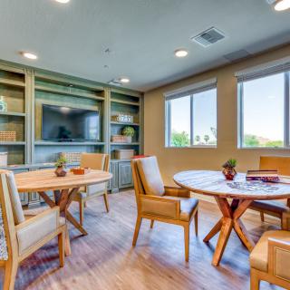 A modern room with wooden tables and chairs, featuring large windows and built-in shelves.
