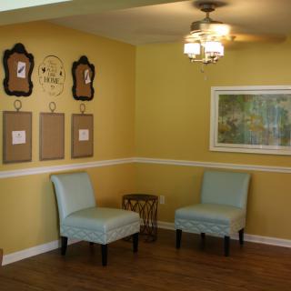 A cozy living room with yellow walls, featuring two chairs, wall art, and a ceiling fan.