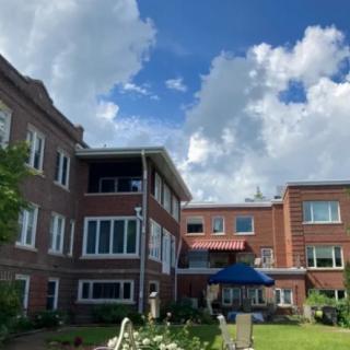 A brick residential building with a garden and cloudy sky.