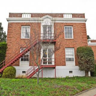 A two-story brick building with external stairs and surrounding greenery.