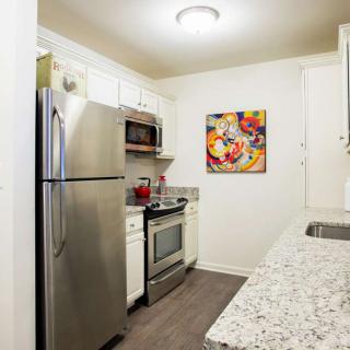 A modern kitchen with stainless steel appliances and white cabinets, featuring colorful artwork on the wall.