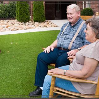 An elderly couple sitting outdoors on wooden chairs, enjoying a relaxing time in the garden.