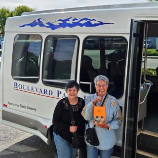 Two individuals stand beside a bus outside, one holding a book.