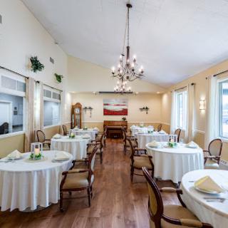An elegant dining area featuring round tables, a chandelier, and warm wooden flooring.