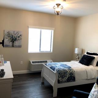 A cozy bedroom featuring a neatly made bed with white furniture and blue accents near a window.