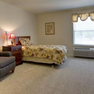 A cozy bedroom with a single bed, armchair, and a large window.
