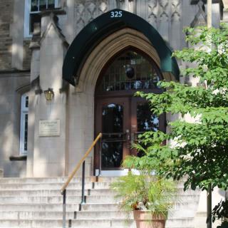 A building entrance featuring an arched doorway and a set of stairs, with a potted plant nearby.