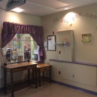 A cozy waiting area in a children's hospital with a table, chairs, and purple curtains.