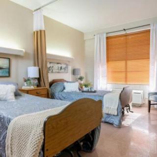 A well-organized hospital room featuring two patient beds separated by a privacy curtain, with bright natural lighting from the window.
