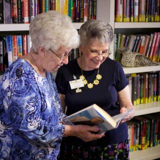 Two women discussing a book in a library setting.