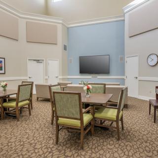 A communal dining area with tables and chairs, featuring a television and wall clock.