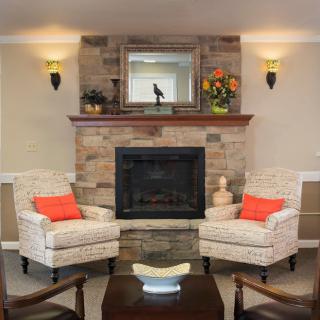 A cozy living room with a stone fireplace, mirrored mantle, and two armchairs adorned with orange cushions.
