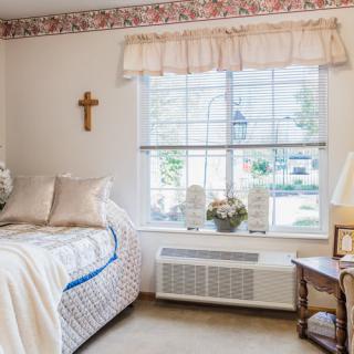 A cozy bedroom with a bed, decorative pillows, and a window with floral curtains.