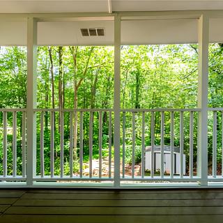A balcony with white railings overlooks a lush, green forest.