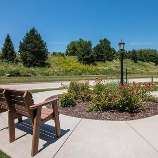 A peaceful garden path with a bench, flowers, and a lamp post under a clear blue sky.
