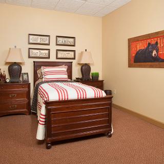 A cozy bedroom featuring a single bed with striped bedding, flanked by nightstands and lamps, along with decorative artwork on the wall.