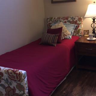 A cozy bedroom with a single bed and a nightstand featuring a lamp.