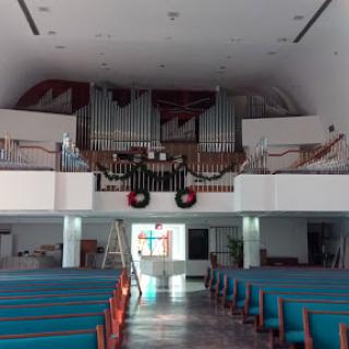 The interior of a church featuring a prominent organ and rows of pews.