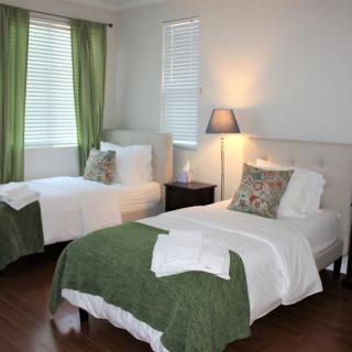 A cozy bedroom with twin beds dressed in green bedding and white sheets, complemented by a nightstand and lamp.