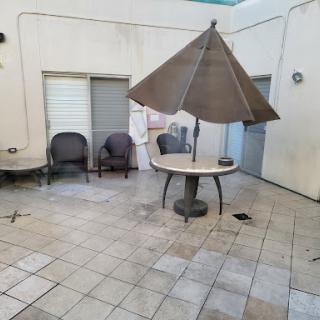 A quiet outdoor patio area featuring a table with an umbrella and chairs, surrounded by tiled flooring.