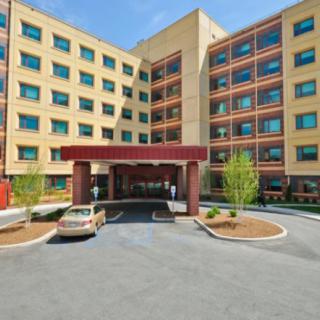 The image shows the front entrance of a hotel with a driveway and parked car.