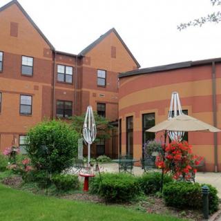 A brick building with a patio area, featuring umbrellas and lush greenery.