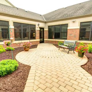 A serene courtyard with a paved path, neatly landscaped plants, and a bench for relaxation.