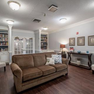 A cozy living room with a brown sofa, hardwood floors, and well-stocked bookshelves.