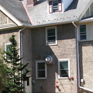A residential house with multiple windows and a sloped roof, partially obscured by a tree.