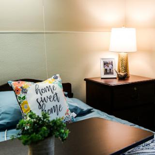 A cozy bedroom setup featuring a beautifully decorated nightstand with a lamp and personal touches.
