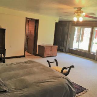 A spacious bedroom with a bed, large windows, and ceiling fan.