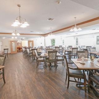 A spacious dining room with multiple tables and chairs, featuring wooden flooring and bright lighting.