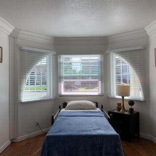 A minimalist bedroom with a single bed, surrounded by large windows letting in natural light.