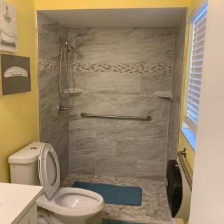 A compact bathroom featuring a tiled shower area with a grab bar, a toilet, and yellow-painted walls.
