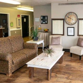 A cozy living room with a sofa, chairs, and a coffee table, decorated with wall art and a clock.