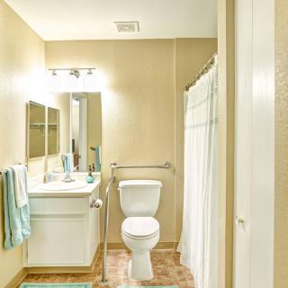 A clean, well-lit bathroom with a toilet, sink, mirror, and shower area.