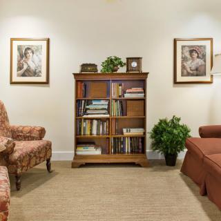 A cozy living room with a wooden bookshelf, armchairs, and framed artwork on the walls.