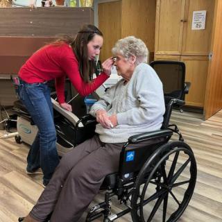 A caregiver assists an elderly person in a wheelchair indoors.