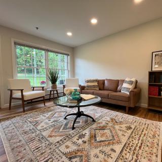 A cozy and modern living room with a sofa, armchair, coffee table, and large window overlooking a green outdoor area.
