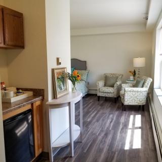 A cozy room with a kitchenette, seating area, and large window allowing natural light.
