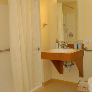 A hotel bathroom featuring a wall-mounted sink, mirror, and shower area with a curtain.