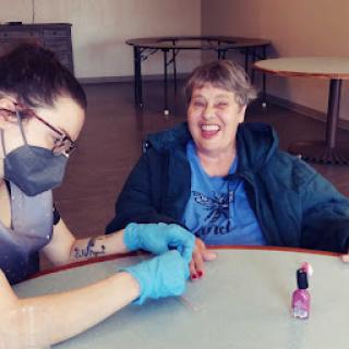A caregiver applying nail polish during a fun activity with a smiling individual.
