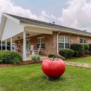A brick house with a well-maintained lawn featuring a large tomato sculpture in the front yard.