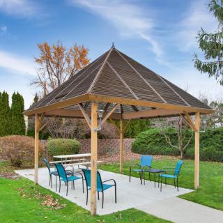A wooden gazebo with blue chairs and a table, set in a park with green grass and surrounding trees.