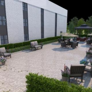 An outdoor patio area with chairs and tables next to a modern building, surrounded by greenery.