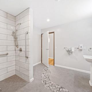 A modern bathroom featuring a walk-in shower with white tiles and accessibility features.