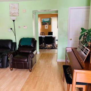 A cozy living room with green walls, featuring leather chairs and a piano, leads into another room.