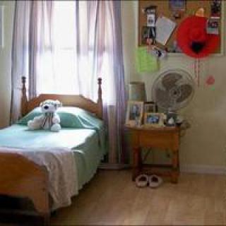 A cozy bedroom with a single bed and stuffed teddy bear by the window, featuring a nightstand with personal items and decorations.