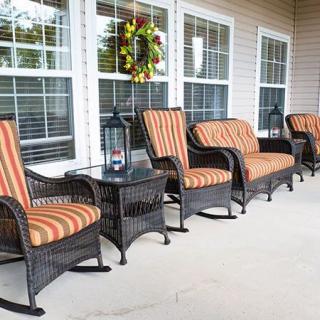 A welcoming porch with wicker chairs and striped cushions, accented by a lantern and decorative wreath.