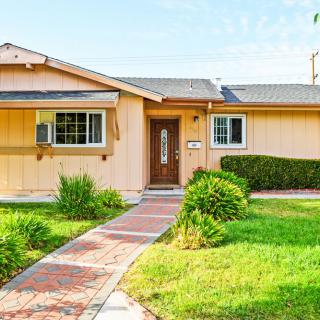 A charming suburban single-story house with a well-maintained lawn and brick pathway.